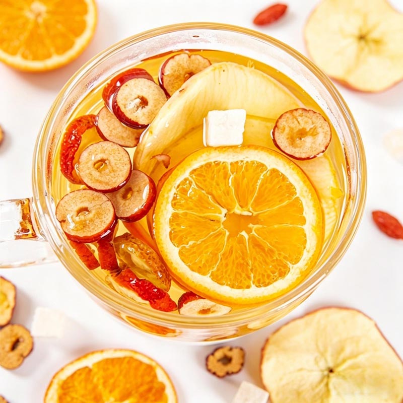 Top view of brewed Apple & Poria Cocos tea with orange slice, apple slice and red date pieces